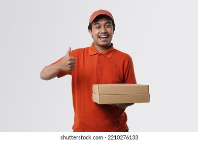 Shipment Concept. Portrait of asian man delivery, wearing red cap and uniform holding cardboard box and showing okay sign gesture standing isolated over white studio