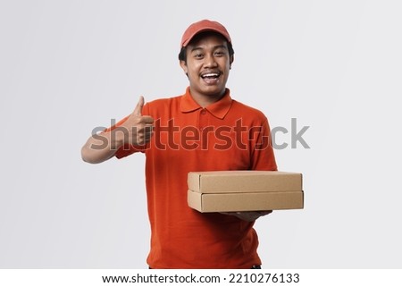 Shipment Concept. Portrait of asian man delivery, wearing red cap and uniform holding cardboard box and showing okay sign gesture standing isolated over white studio