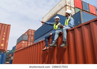 Shipment worker use a walkie-talkie to point to container storage location, explain to colleague about planning for next shipment. Young worker with safety vest holding tablet computer sit beside him - Powered by Shutterstock