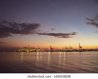 Shipping cranes at a port by the sea looking like metal giraffes during sunrise or sunset