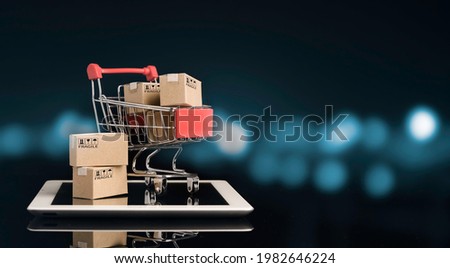 Shipping paper boxes inside Red shopping cart trolley on tablet with black and blue bokeh background and copy space , Online shopping and e-commerce concept.