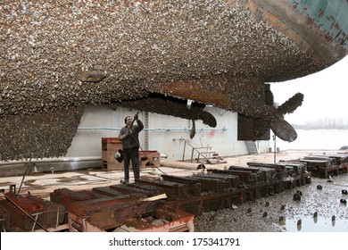 Shipyard worker cleans the ship stuya water from vegetation and mussels
