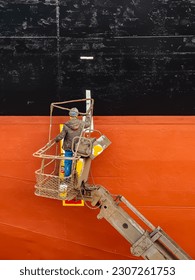 A shipyard worker on a cherry picker is painting on a ship side