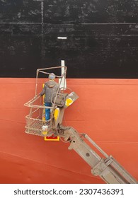 A shipyard worker on a cherry picker is painting on a ship side