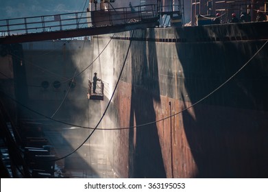 Shipyard Worker Power Washing A Ship On Dry Dock.