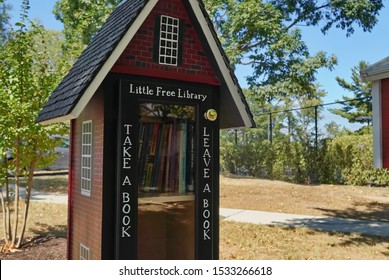 Shirlington, VA / USA - September 24, 2019: Little Free Library Book Exchange Box Shaped Like A Schoolhouse Full Of Childrens Books In The Middle Of A Residential Neighboorhood