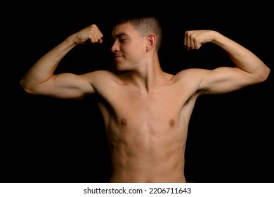 Shirtless 19 year old teenage boy flexing his arm muscles on a black background - Shutterstock ID 2206711643