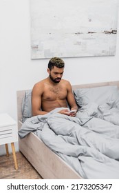 Shirtless African American Man With Dyed Hair Chatting On Mobile Phone In Bed