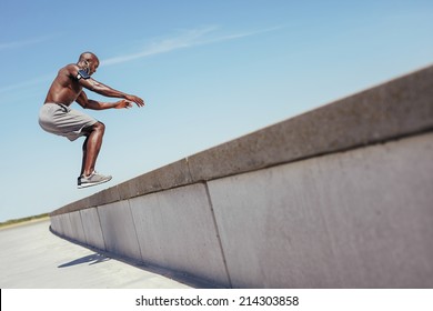 Shirtless African Athlete Working Out On Cross Fit Jump Box Outside On A Wall. Muscular Man Doing Box Jumps Outdoors.