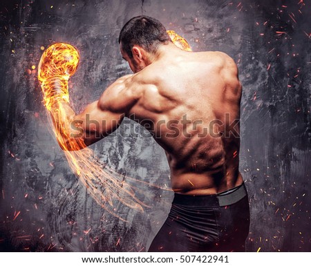 Shirtless aggressive fighter with burning boxer gloves on grey background.