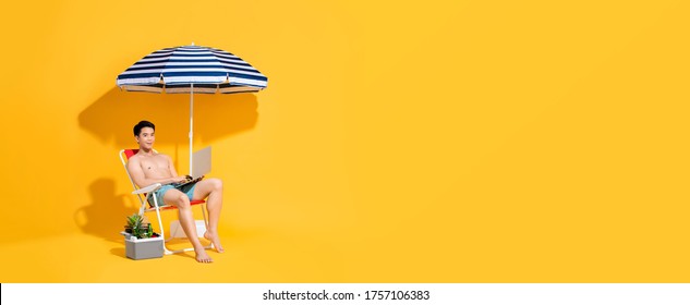 Shirtless Asian Man Working  On Laptop Computer While Sitting On Beach Chair With Umbrella Isolated On Yellow Banner Backgound With Copy Space For Summer Vacation Concept