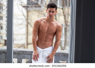 Shirtless, athlete handsome man poses on balcony with naked torso in outside.