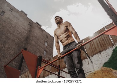 Shirtless athlete practicing calisthenics with smartwatch on his wrist. Young man doing horisontal bar muscle ups exercise. Outdoor workout. Fitness gadgets concept. Space for text. - Powered by Shutterstock