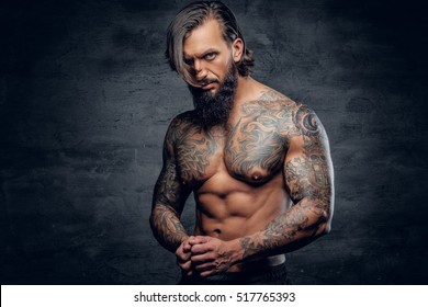 Shirtless athletic bearded hipster male with tattooed muscular body on grey vignette background.