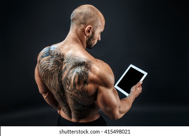 Shirtless Bald Tatooed Man Using Tablet Stand Back