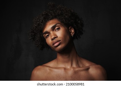 Shirtless black man with piercing posing and looking at camera isolated over dark background