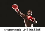 A shirtless boxer throws a punch with red boxing gloves in a dark studio.