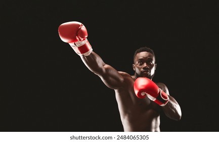 A shirtless boxer throws a punch with red boxing gloves in a dark studio. - Powered by Shutterstock