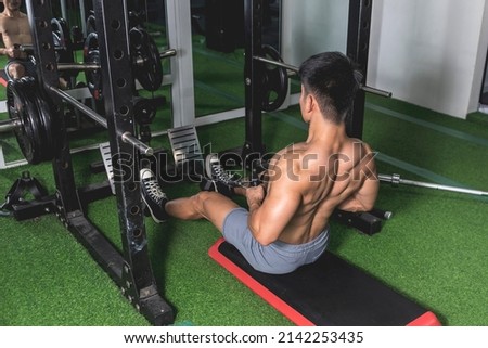 A shirtless and buff asian man does a set of seated V-bar cable rows at the gym. Rowing machine exercise to train and develop back muscularity and mass.