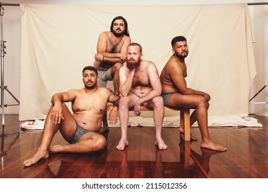 Shirtless and confident. Four body positive men looking at the camera while wearing underwear in a studio. Group of self-assured men embracing their natural bodies together.