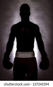 Shirtless macho man wearing boxing gloves posing in dark.