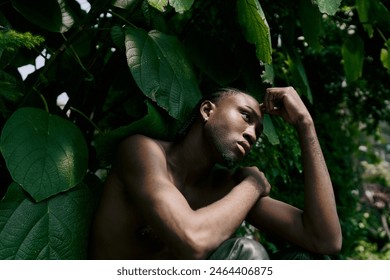 A shirtless man with dapper style posing peacefully in a vivid green garden.
