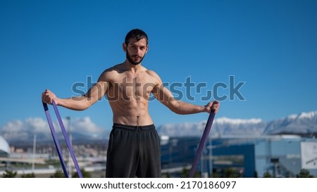 Shirtless man doing exercise with rubber bands outdoors. 