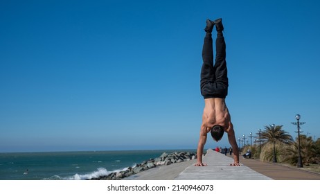 Shirtless man doing a handstand on the seashore. 