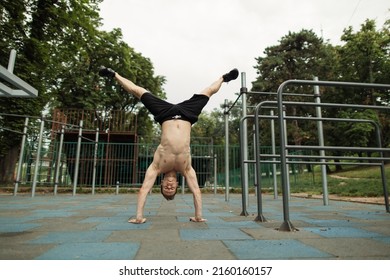 Shirtless man doing a handstand on the outdoor gym. Shirtless man walks on his hands outdoors. Outdoor gym. Healthy lifestyle. Sport. Hobby. Muscular body.