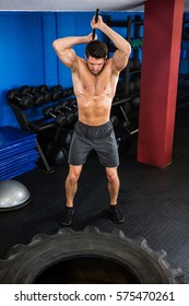 Shirtless Man Doing Sledgehammer Swing Exercise In Fitness Studio