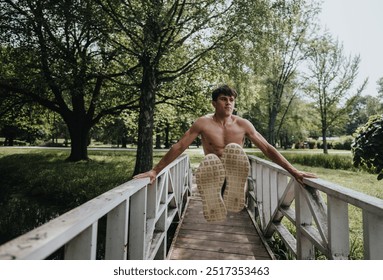 A shirtless man executing a dynamic parkour jump on a bridge in a sunny park, surrounded by lush greenery and trees. - Powered by Shutterstock