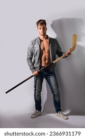 A shirtless man holding a hockey stick and a hockey puck