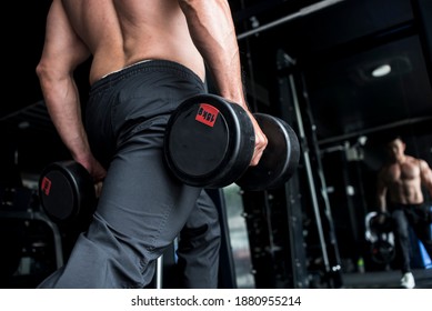 A Shirtless Man Holds 2 Rubberized Dumbbells While Doing Dumbbell Lunges At A Gym Or Fitness Center.