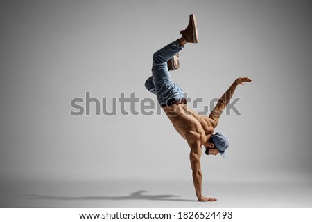 Shirtless man in jeans doing a handstand isolated on gray background