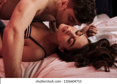 ネオンの赤い光でベッドの美しい女性にキスをする、シャツのない男性