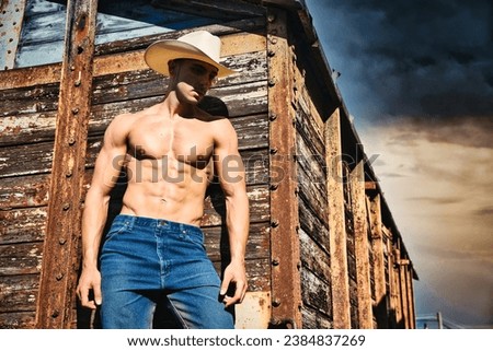 A shirtless man standing in front of an old rugged wooden train wagon