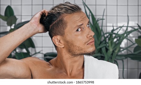 Shirtless Man Styling Hair Near Green Plants On Blurred Background In Bathroom 