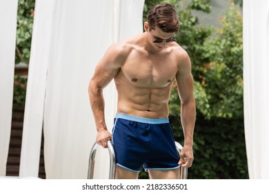 Shirtless Man In Sunglasses And Swimming Shorts Near Pool Ladder