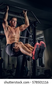 Shirtless Muscular Man Doing ABS Workouts On Pull Up Bar In A Gym.