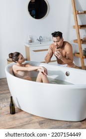 Shirtless Muscular Man Lighting Cigarette Near Sexy Girlfriend Relaxing In Bathtub