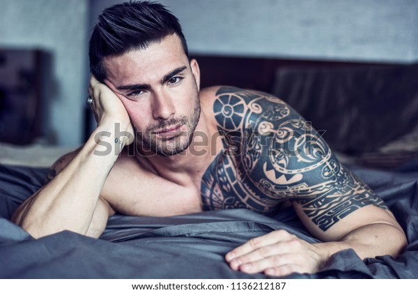 Shirtless Muscular Sexy Male Model Lying Alone On Bed In His Bedroom Looking At Camera With A