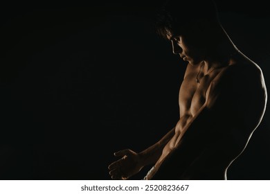 Shirtless muscular young man posing in low light, showcasing his defined physique and strength. Dark and dramatic lighting creates a moody and intense atmosphere. - Powered by Shutterstock