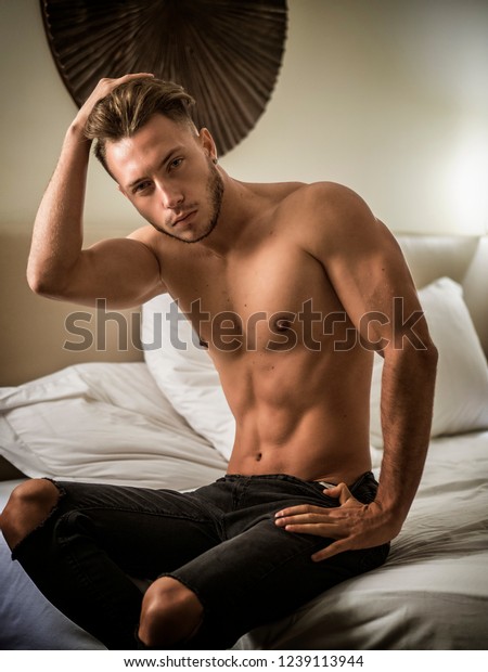 Shirtless sexy male model lying alone on his bed in his bedroom ... photo image