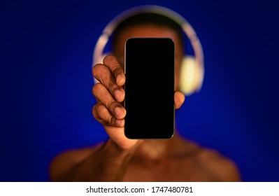 Shirtless Sporty Guy Showing Blank Smartphone Screen Recommending Music App Posing On Blue Studio Background. Fitness Application. Mockup, Selective Focus