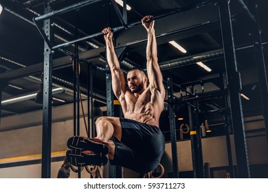 Shirtless Sporty Male Doing ABS Workouts On Pull Up Bar In A Gym Club.