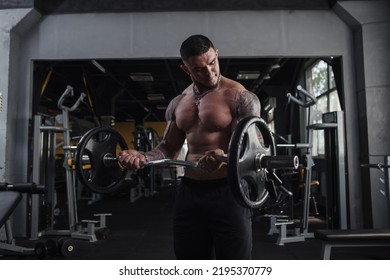 Shirtless tattooed ripped bodybuilder lifting barbell, doing biceps exercise