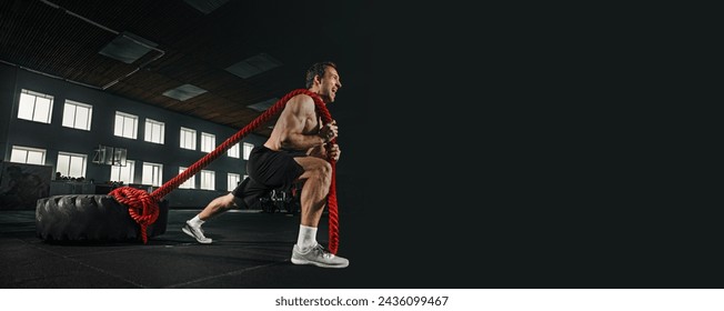 Shirtless young fit man with muscular athletic body pulling heavy tire with rope at gym. Concept of fitness, sport, workout, athlete, power, training, bodybuilding. Banner. Empty space to insert text - Powered by Shutterstock