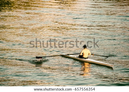 Shirtless young man rowing a single white sculling boat in the Potomac river during a fall golden hour, Washington D.C. 