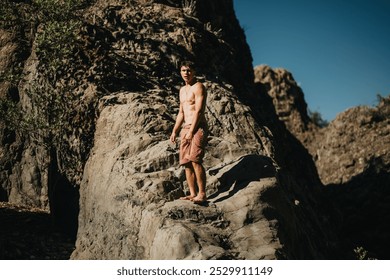 Shirtless young man wearing red shorts exploring rocky terrain in the mountains on a sunny day. Outdoor adventure and nature exploration. - Powered by Shutterstock