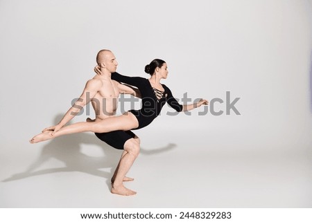 A shirtless young man and a young woman perform acrobatic dance moves in a studio setting against a white background.